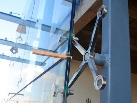 Detailansicht einer Spinnenklaue aus Edelstahl, die zur Unterstützung der Struktur einer großen Glaswand verwendet wird.